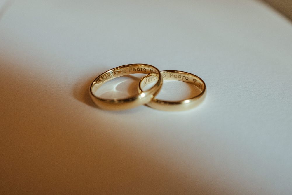 Two gold wedding bands with engraved inscriptions resting together on a soft white surface.