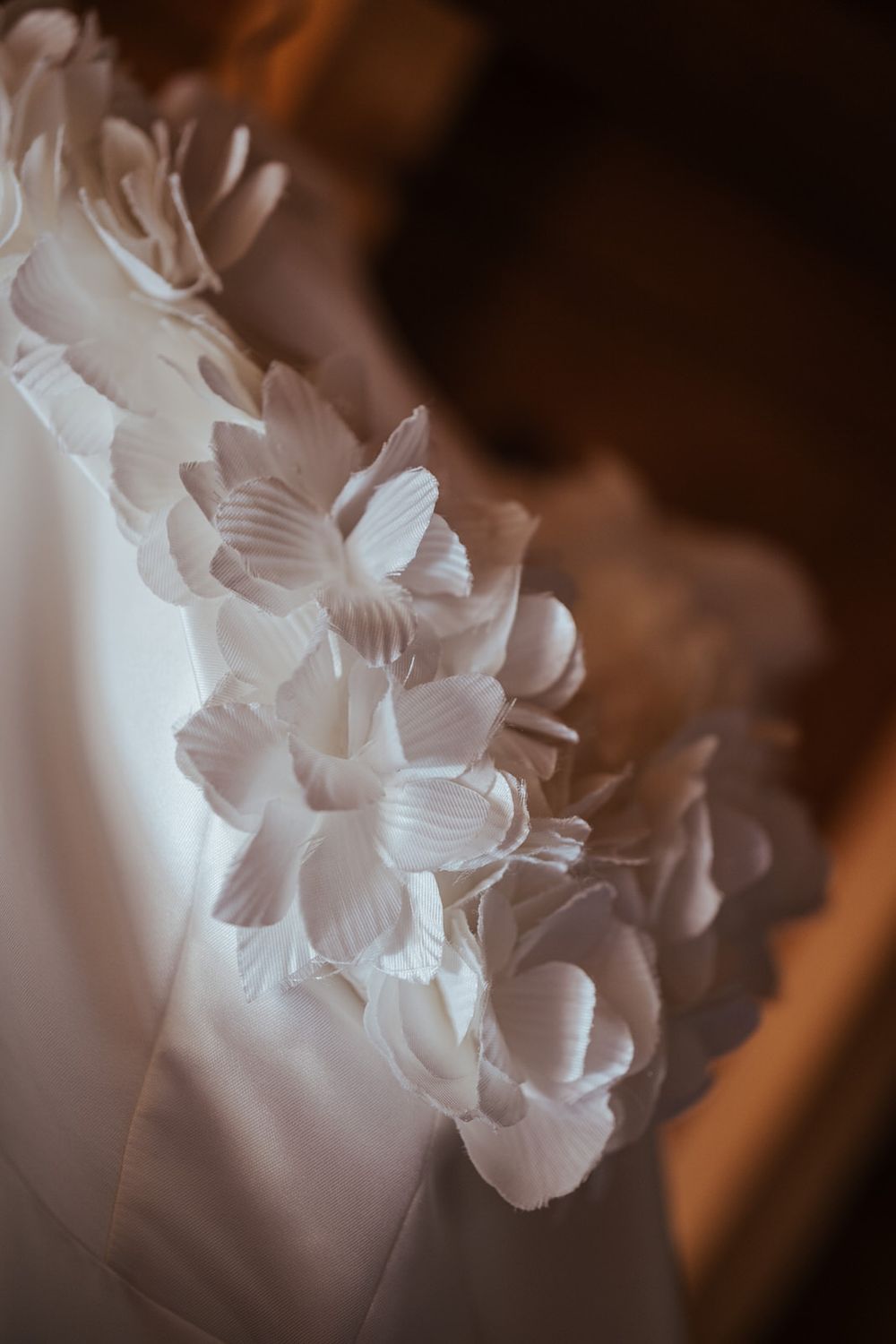 Close-up of a white wedding dress adorned with delicate 3D floral petal embellishments along the neckline.