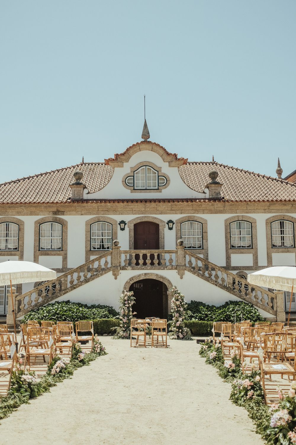 Stunning outdoor wedding ceremony setup at a classic Portuguese manor with wooden chairs lining a floral aisle.