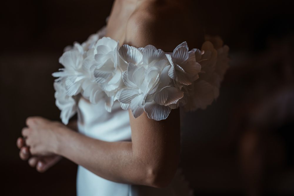 Close-up of a bride wearing an elegant off-shoulder wedding dress adorned with delicate 3D floral petal details.