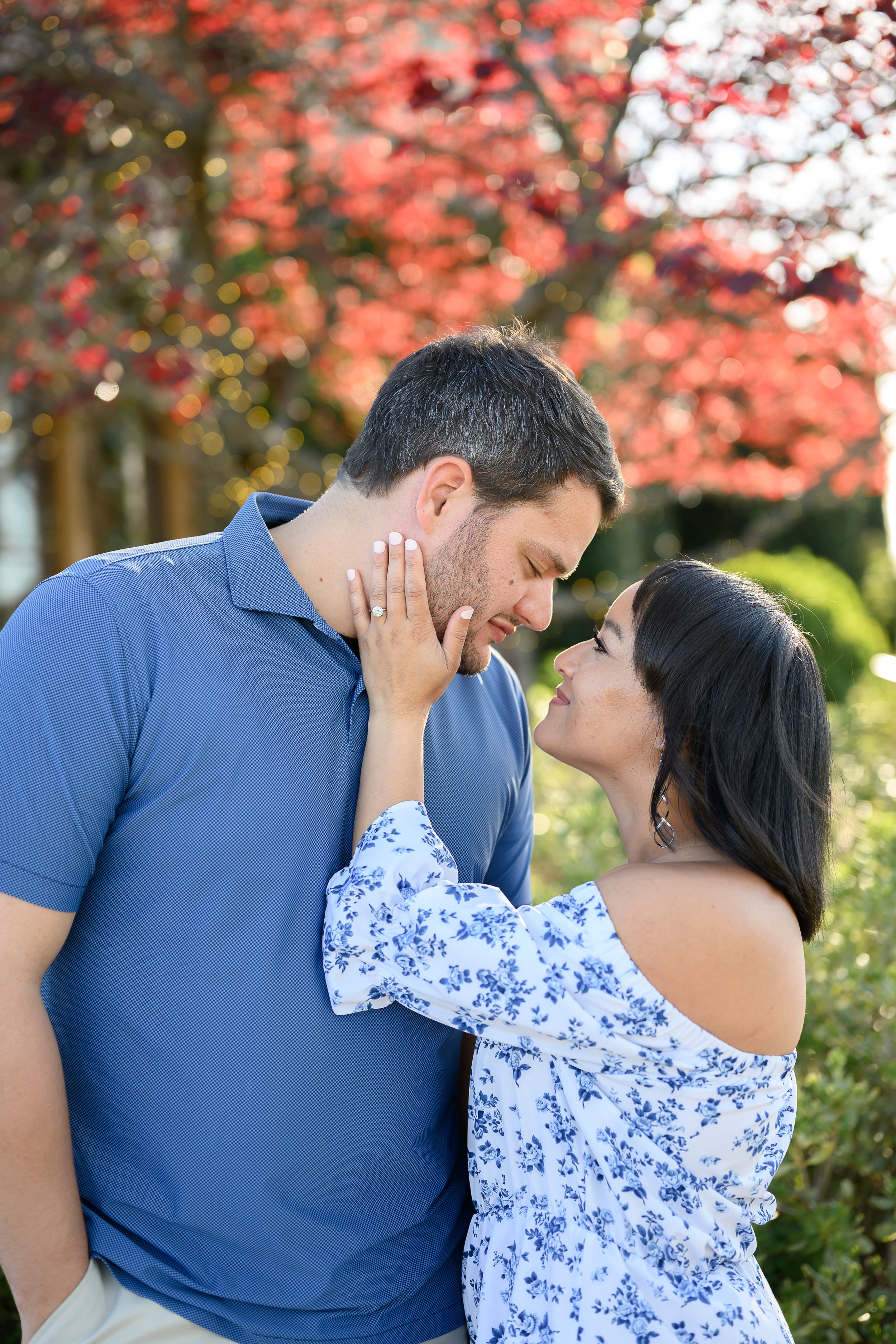 Couple sharing a romantic moment outdoors with vibrant red autumn foliage in the background.