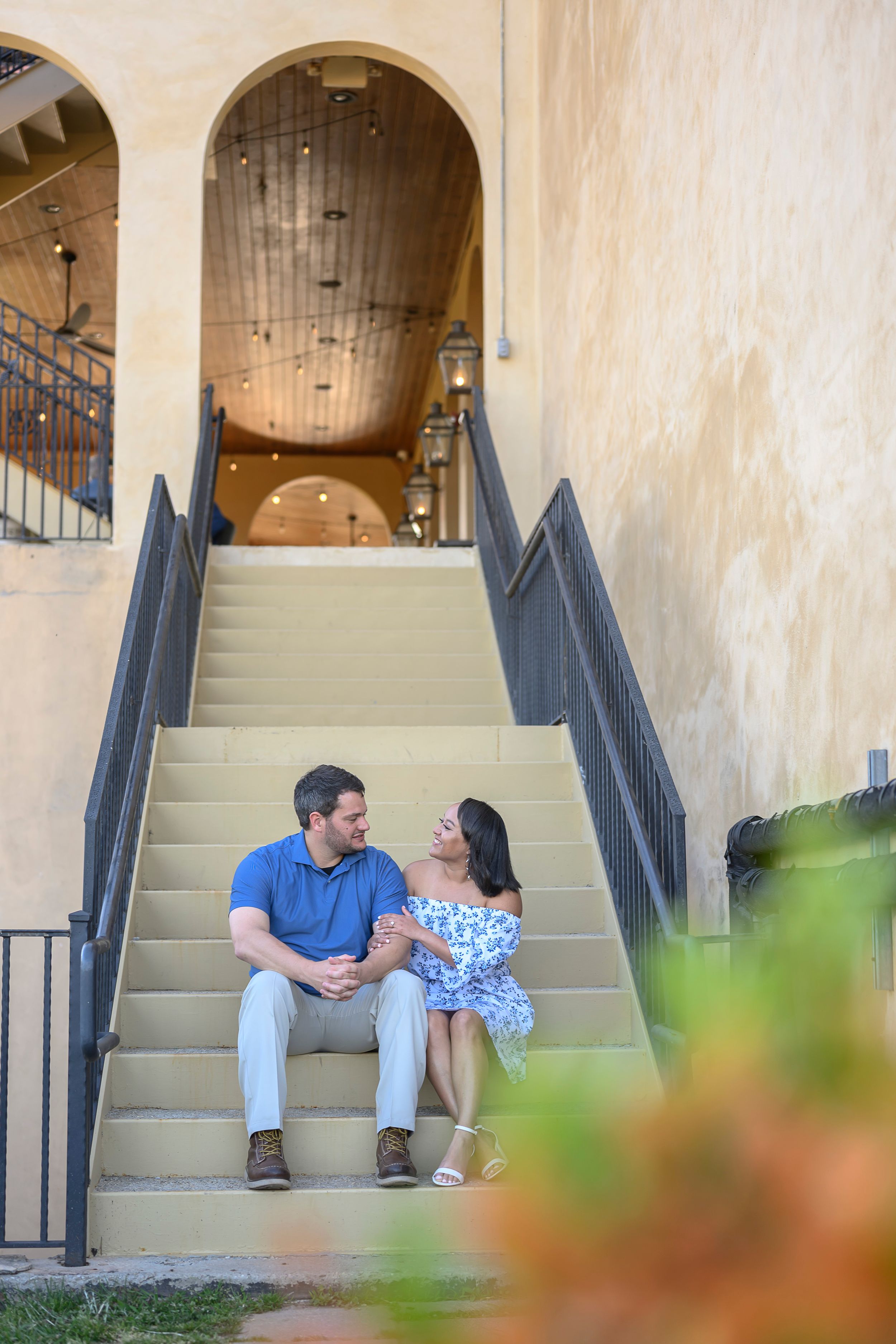Couple sitting together on outdoor stairs of a Mediterranean-style building, sharing a romantic moment.