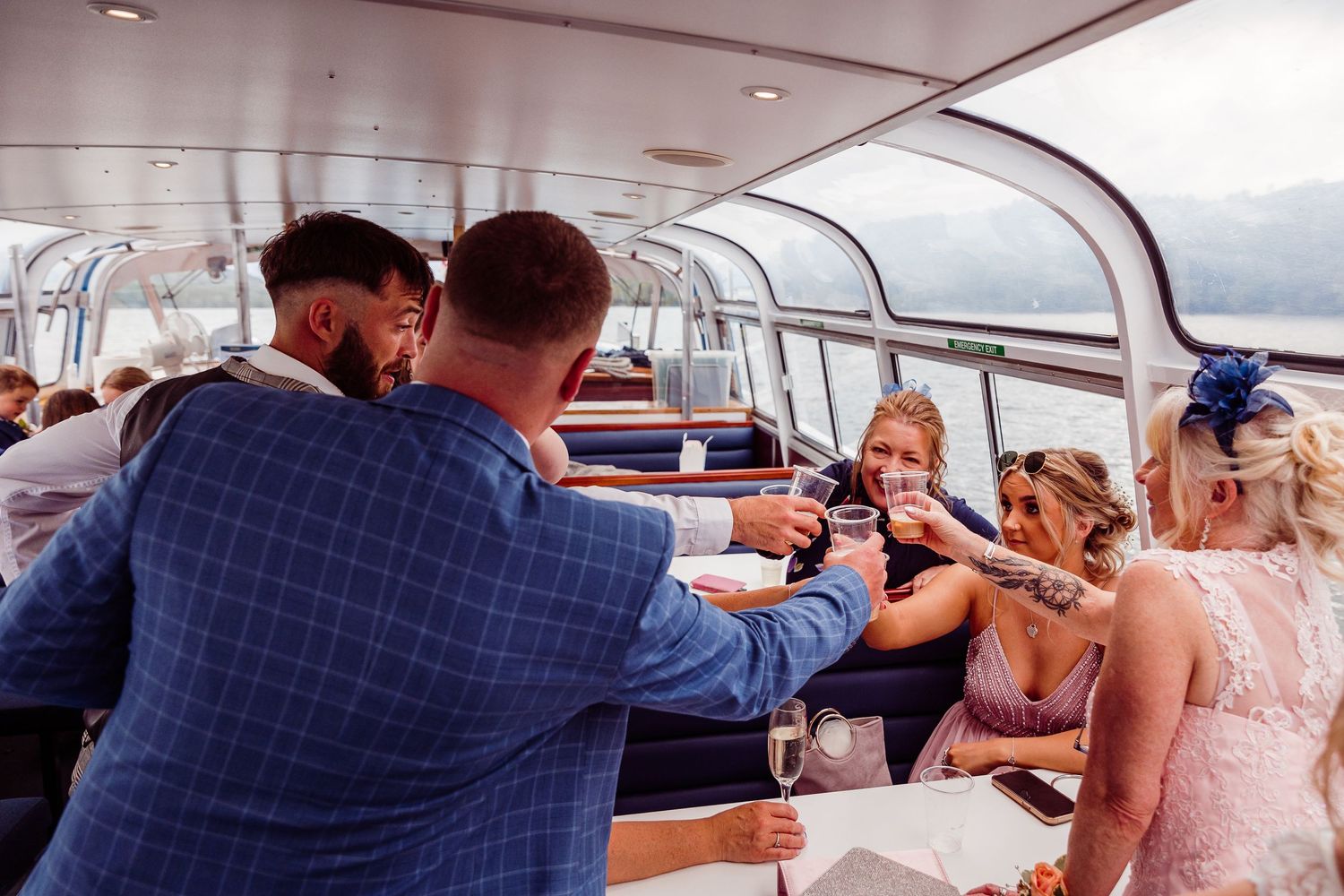 Wedding guests toasting with champagne glasses on a scenic boat cruise, celebrating in formal attire.
