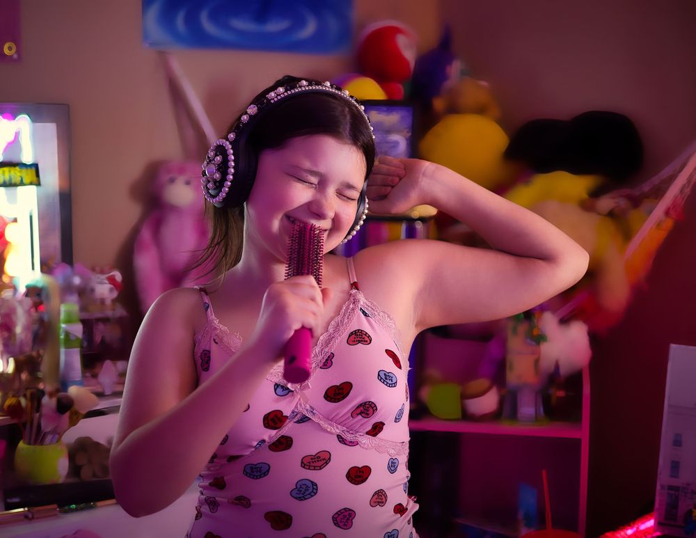 Young girl in pajamas enjoying a popsicle while wearing headphones in a colorful room.