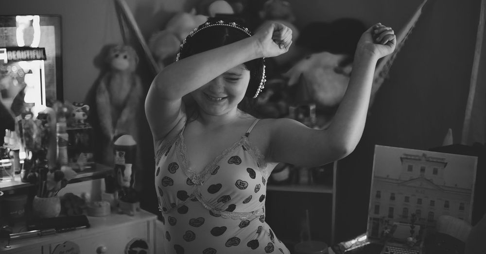 A young girl dances joyfully with arms raised in a black and white photo.