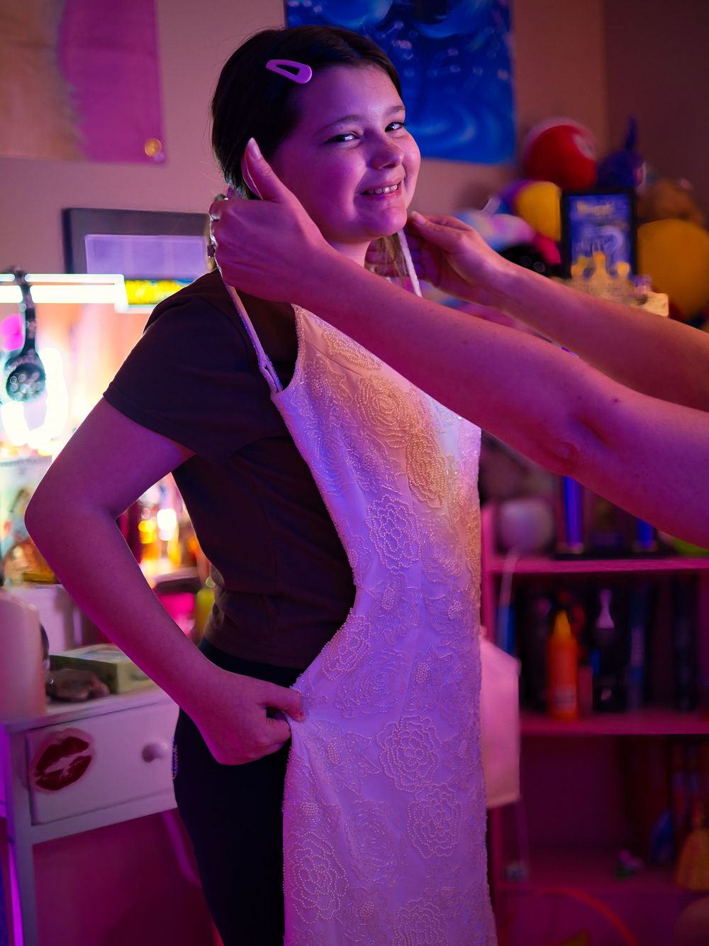 A young girl smiles as someone places a necklace around her neck in a colorful room.