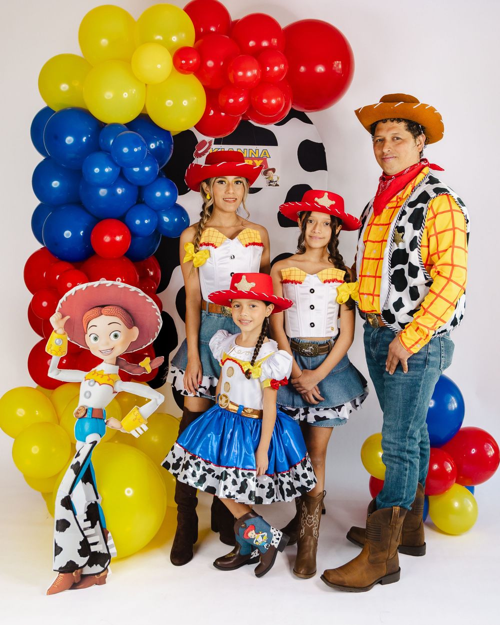 Family dressed as Toy Story characters Woody and Jessie pose with colorful balloons at a themed birthday party.