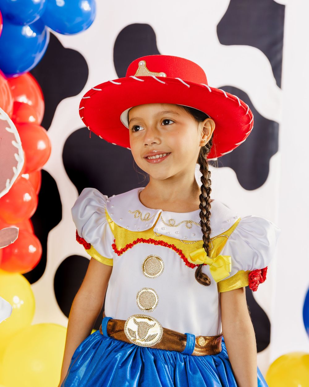 Young girl dressed as Jessie from Toy Story in red cowboy hat, braids, and colorful costume at a themed party.