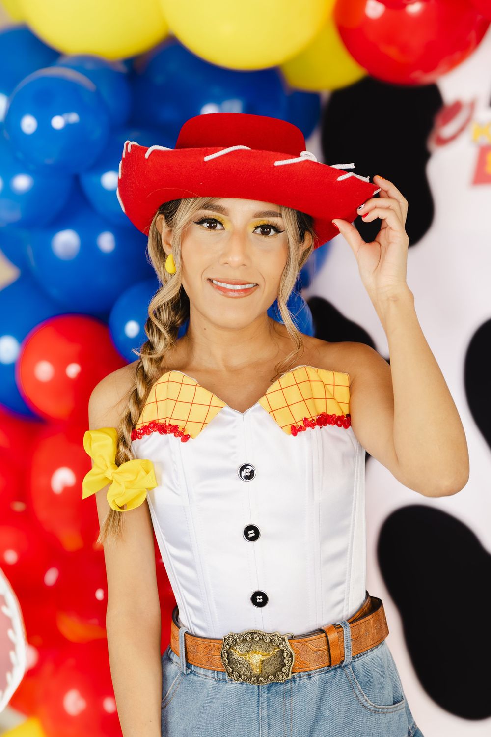 Woman in Jessie from Toy Story costume with red cowboy hat, white corset, and jeans, posing with colorful balloons.