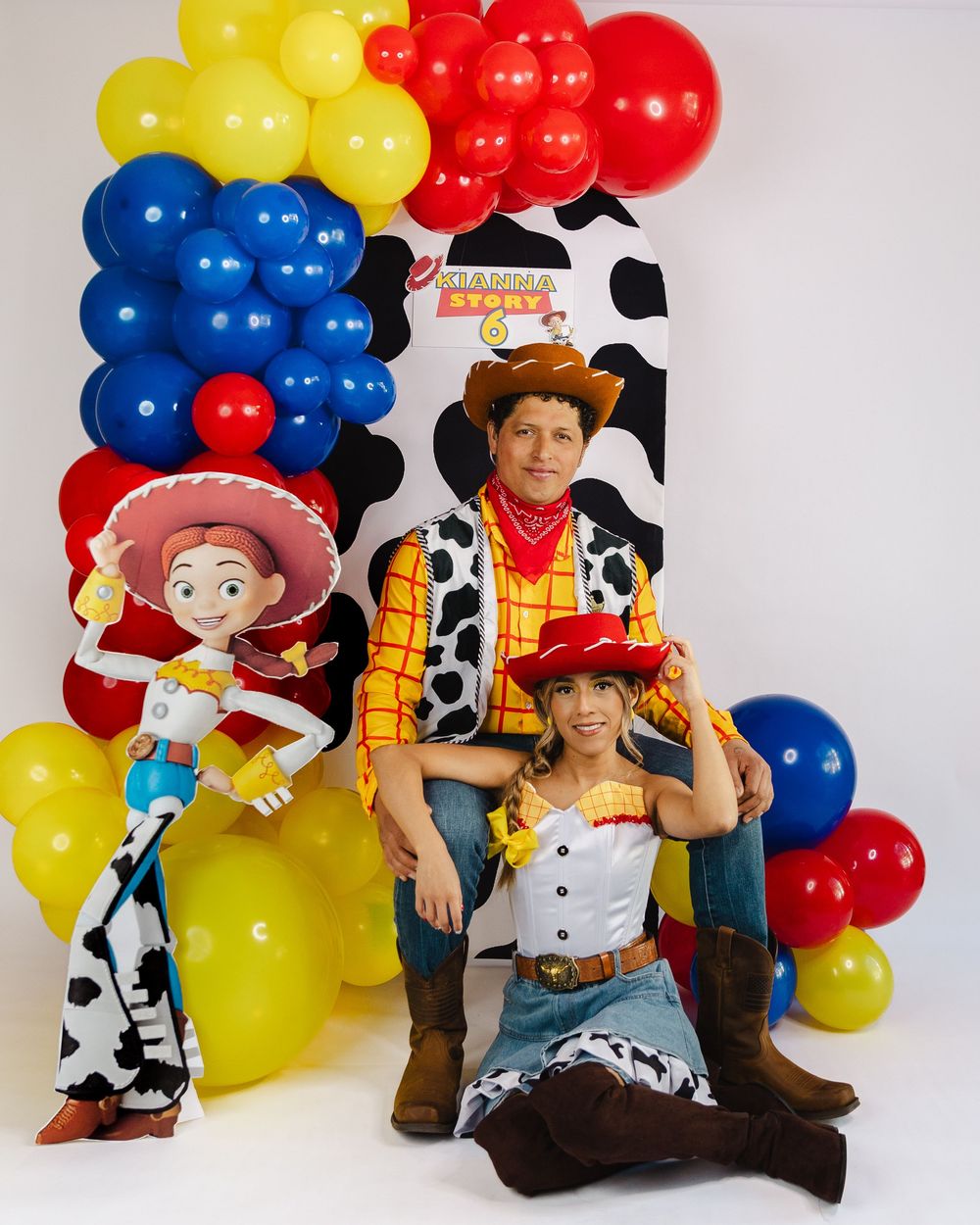 Man and girl in Toy Story Woody and Jessie costumes pose at a colorful balloon backdrop birthday party.