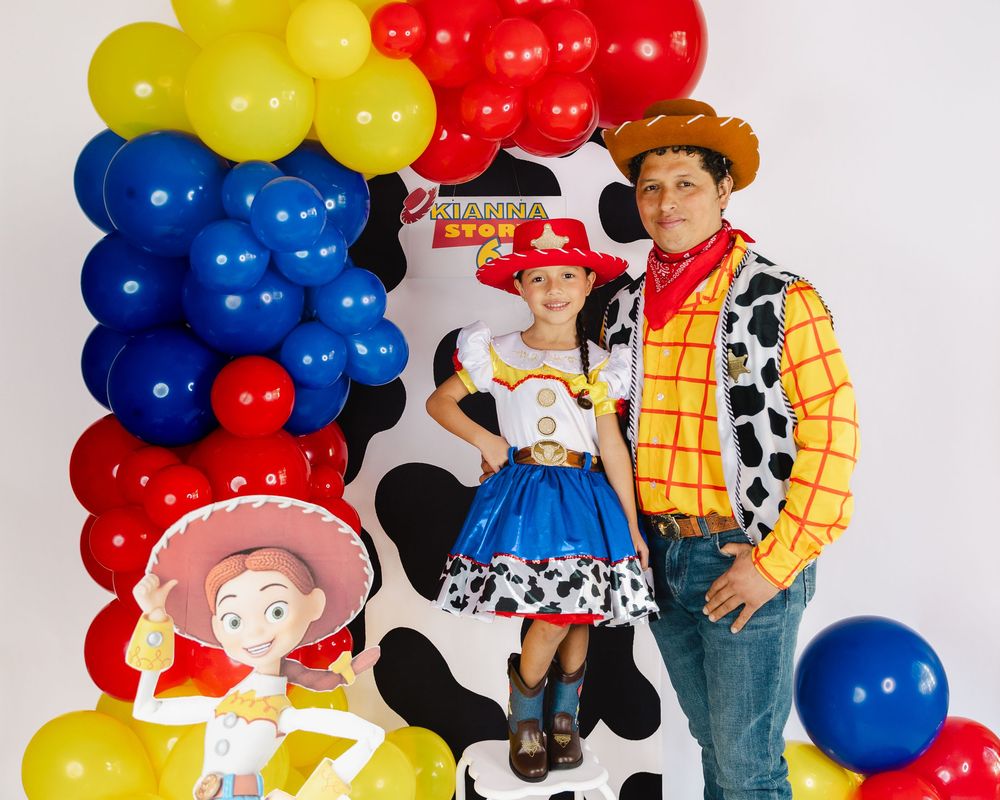 Man and girl in Toy Story Woody and Jessie costumes pose by colorful balloon arch at themed birthday party.