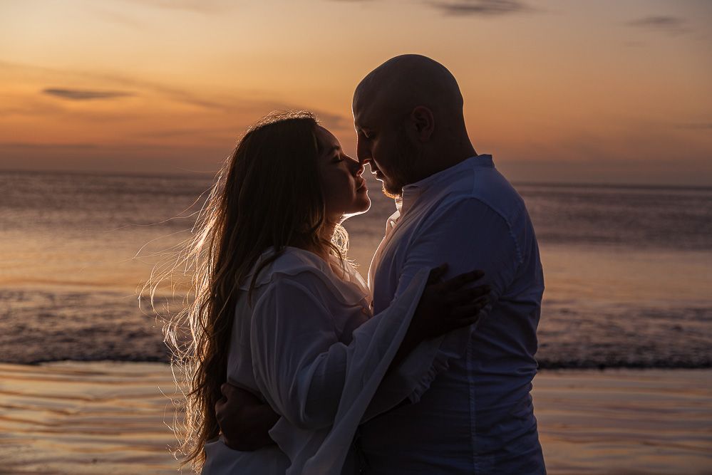 Romantic couple embracing at sunset on a beach, silhouetted against golden ocean waves.