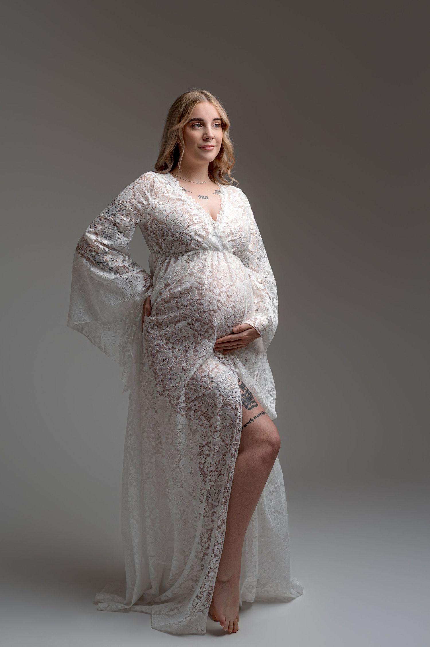 A maternity portrait showing an expecting mother in a flowing teal dress against a dark backdrop.