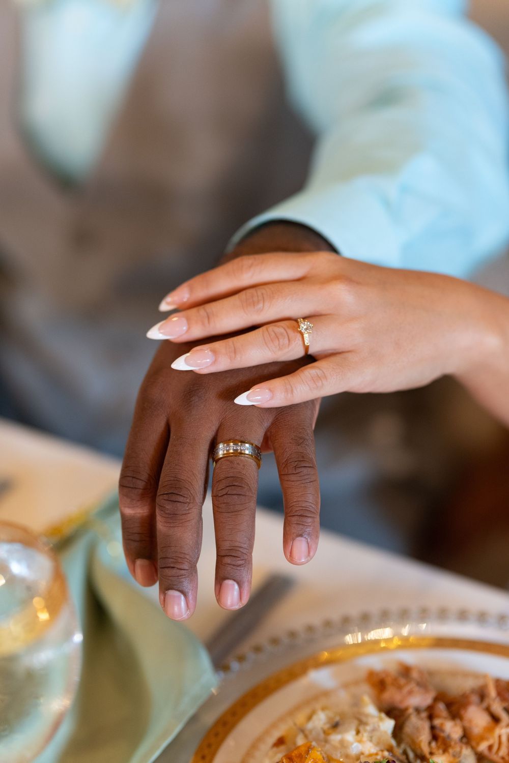 Close-up of interracial couple's hands showing wedding rings at a decorated reception dinner table.