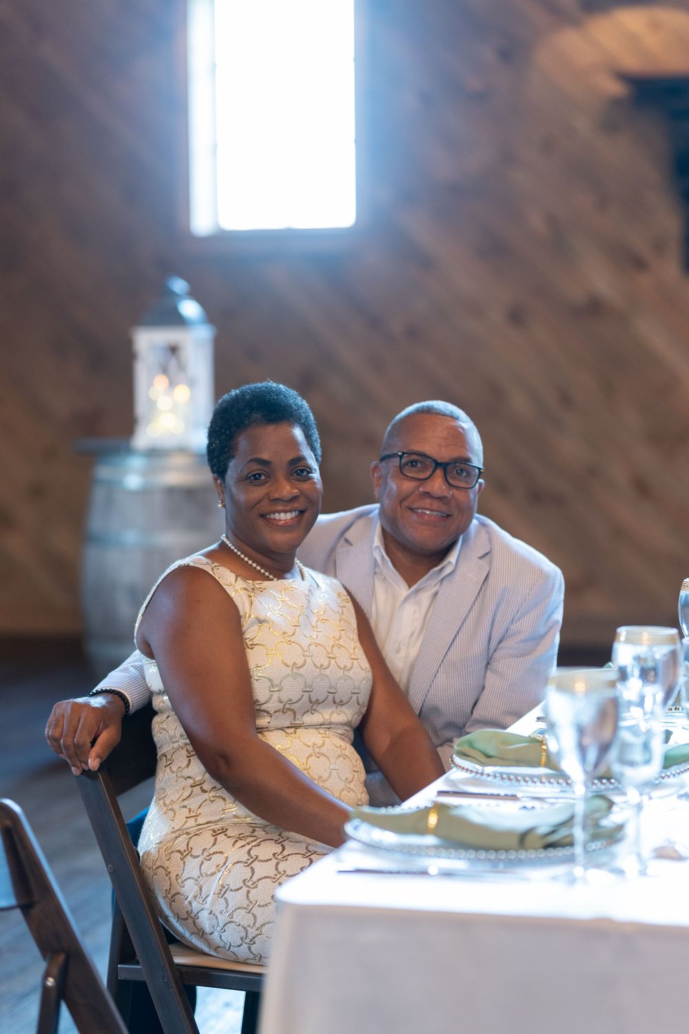 Smiling couple posing together at a elegantly set table during a wedding reception in a rustic venue.
