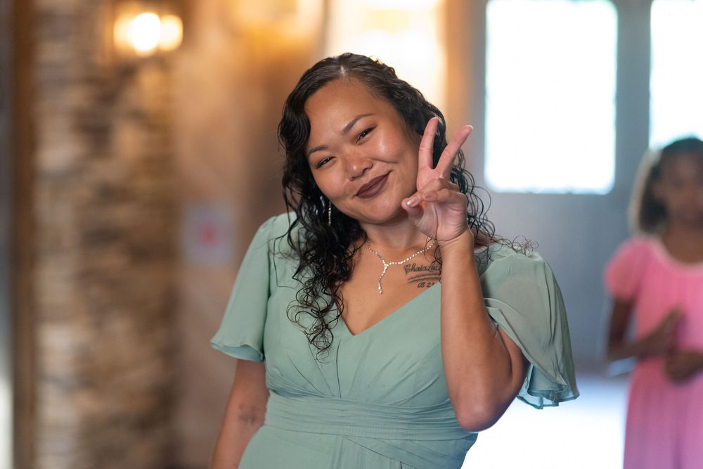Woman in mint green dress smiling and making a peace sign gesture at a wedding reception.