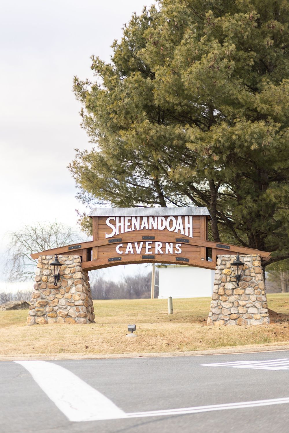 Shenandoah Caverns entrance sign with stone pillars and wooden arch, surrounded by trees in Virginia.