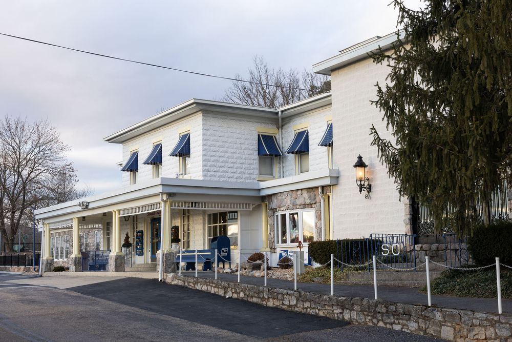 White two-story building with blue awnings and stone wall, serving as a charming restaurant or shop in a suburban setting.
