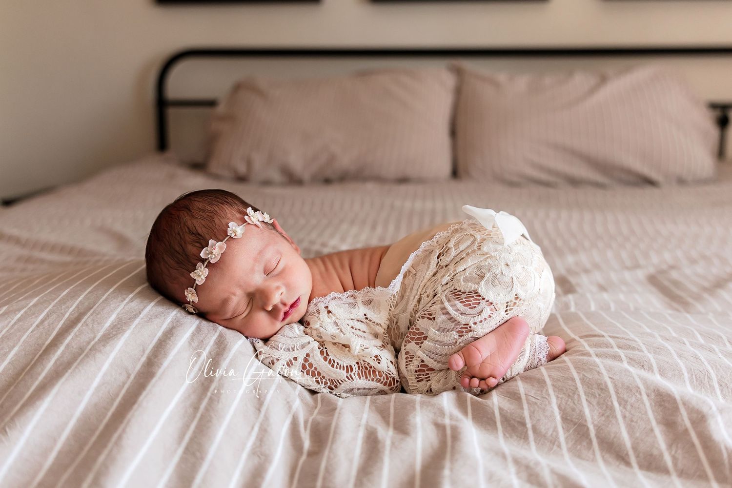 Newborn baby girl sleeping peacefully on a bed wearing a lace outfit and floral headband.
