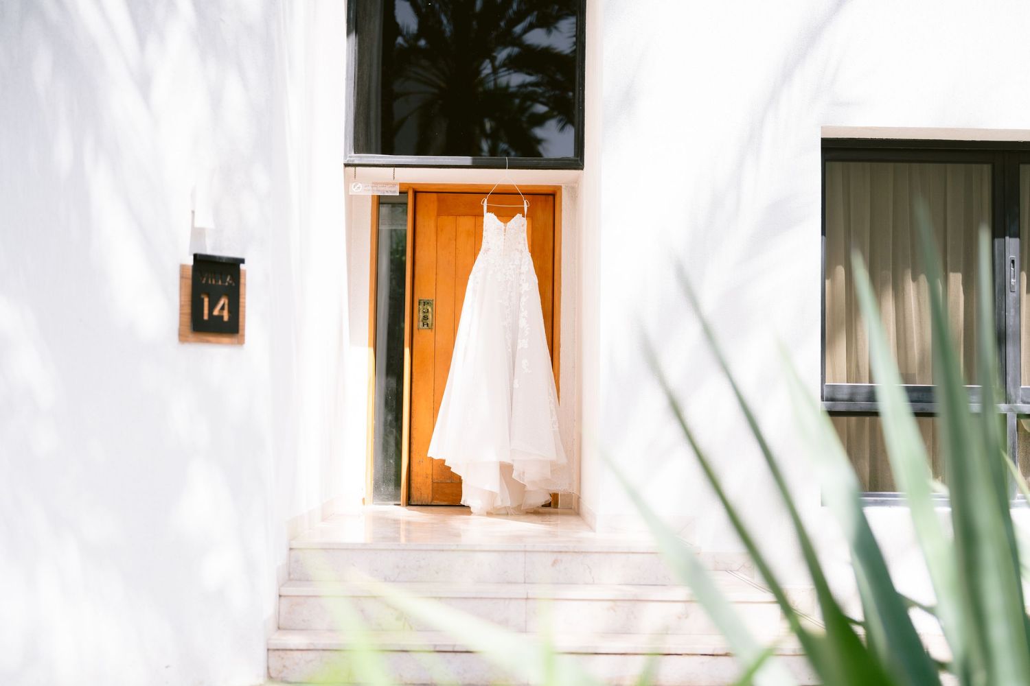 A white wedding dress hanging in an open doorway of a villa numbered 14, with shoes placed below it.