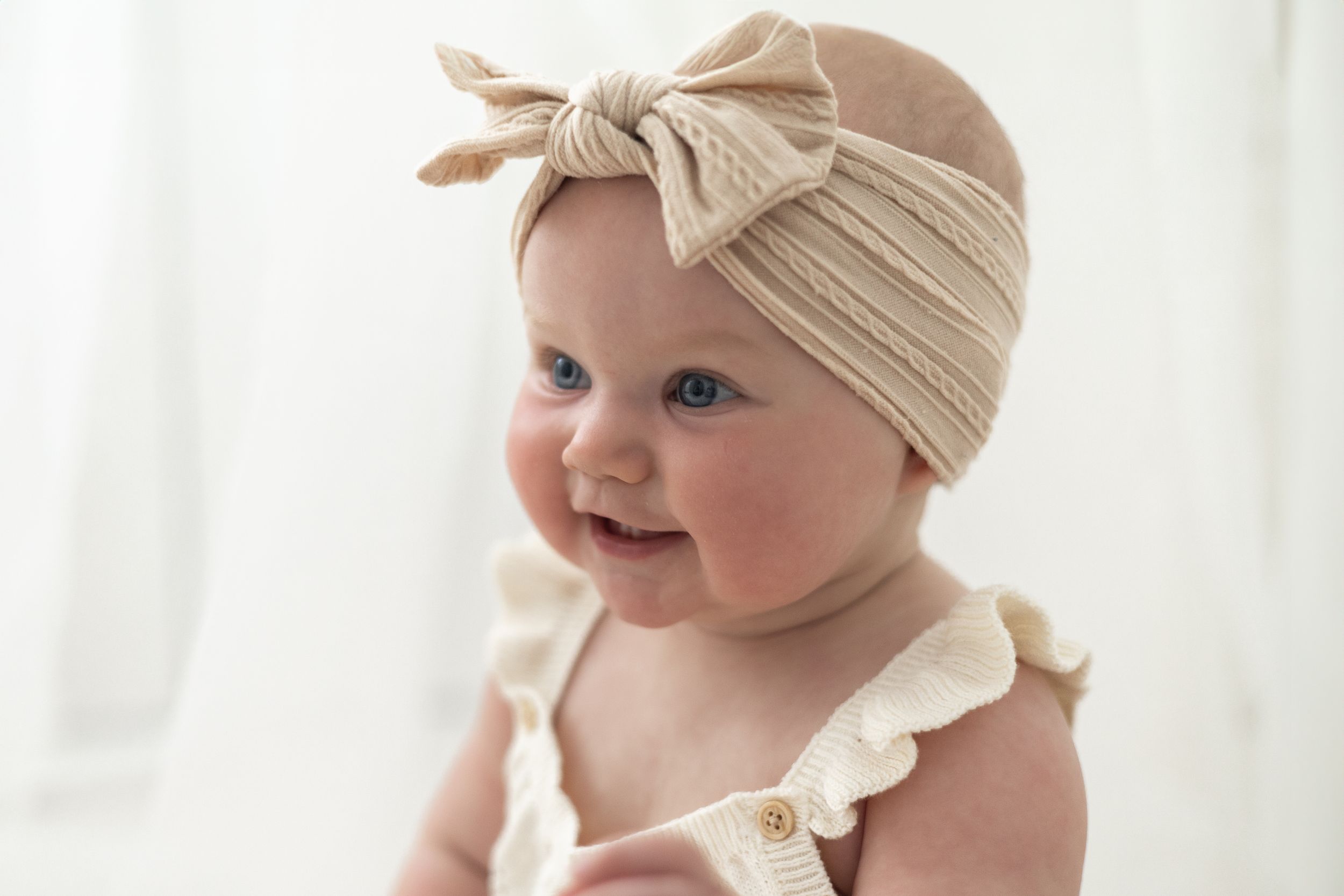 Smiling baby wearing a beige knit bow headband and ruffled romper,  Milestone photoshoot Nottingham
