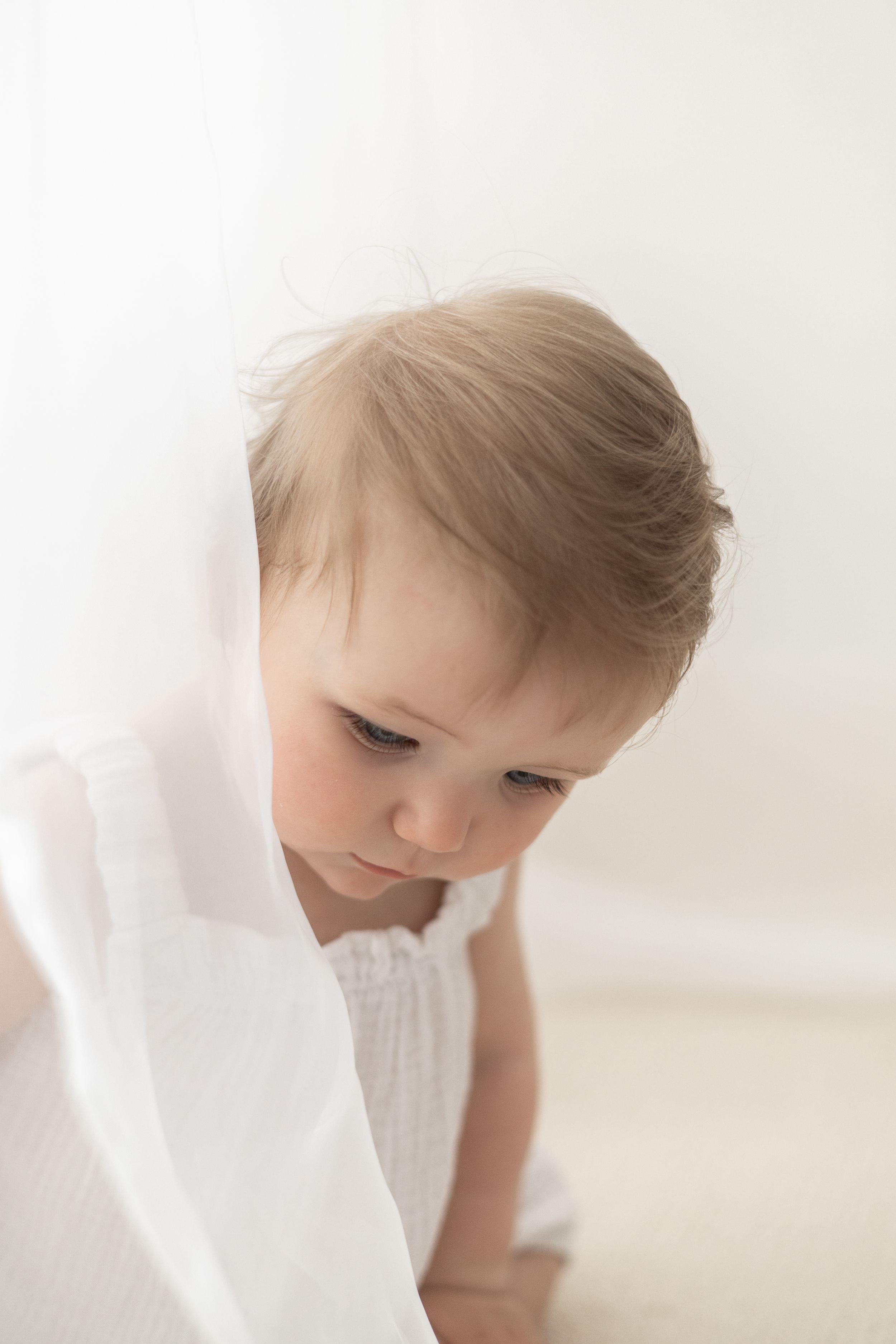 Adorable baby girl in white dress looking down, Nottingham baby milestone session first birthday photography