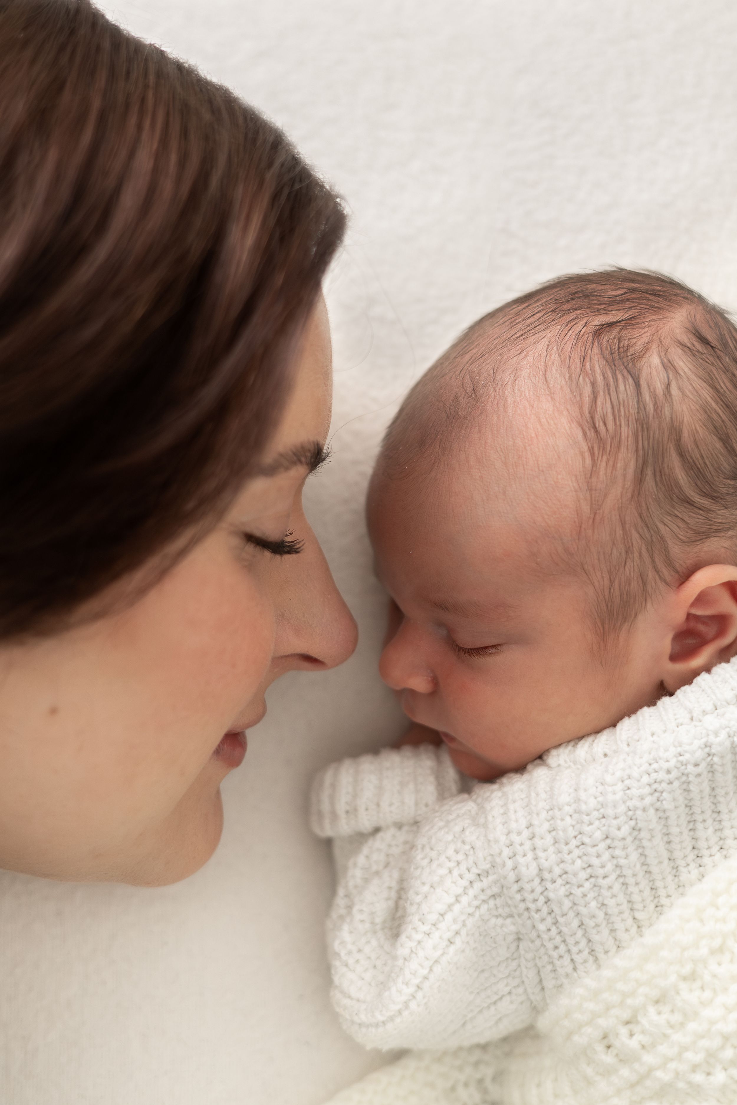 A mother and newborn baby lying face to face on a white blanket, sharing a tender moment. during newborn photoshoot based in Nottingham