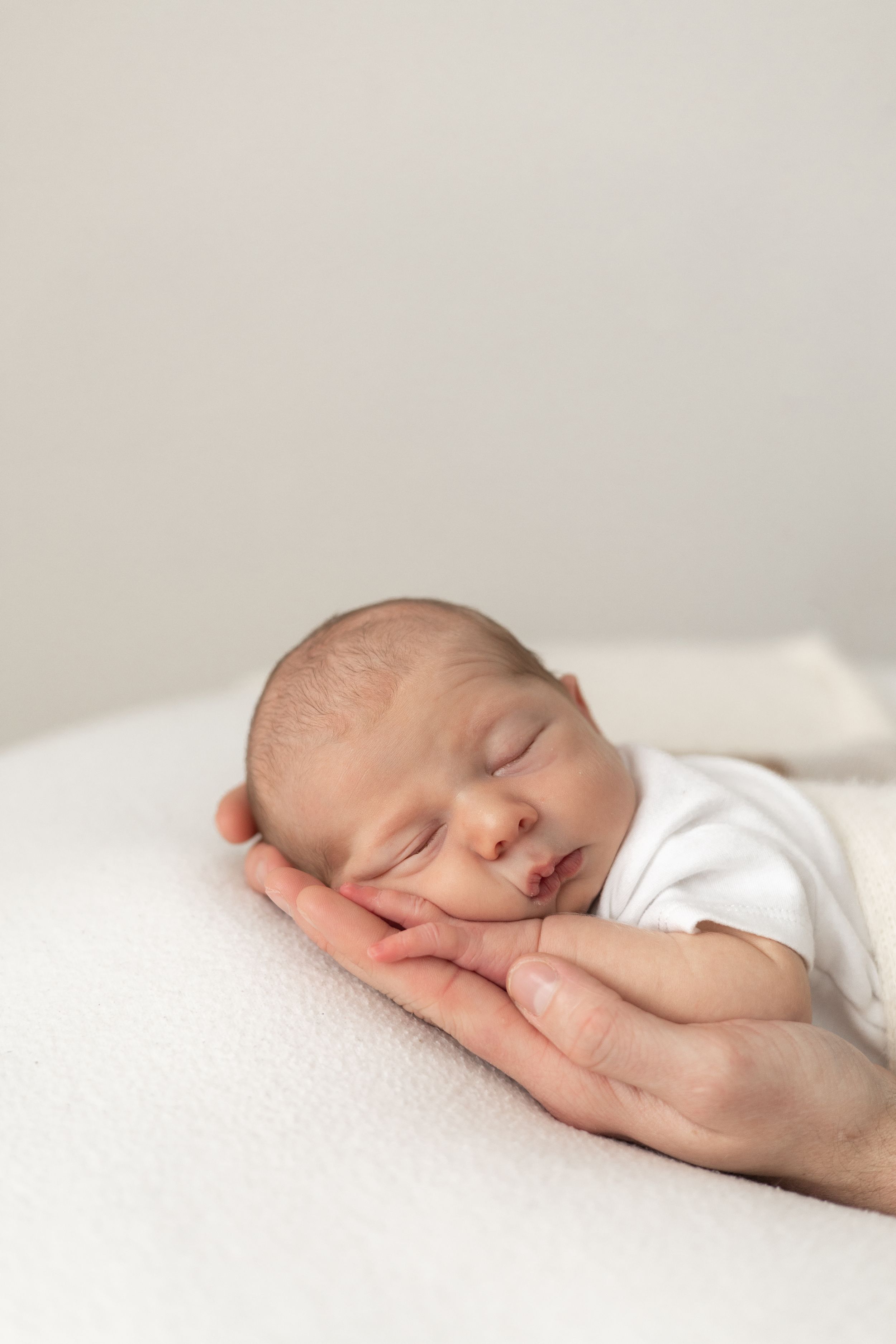 Newborn baby sleeping peacefully on parent's hand on white blanket relaxed newborn photoshoot Nottingham