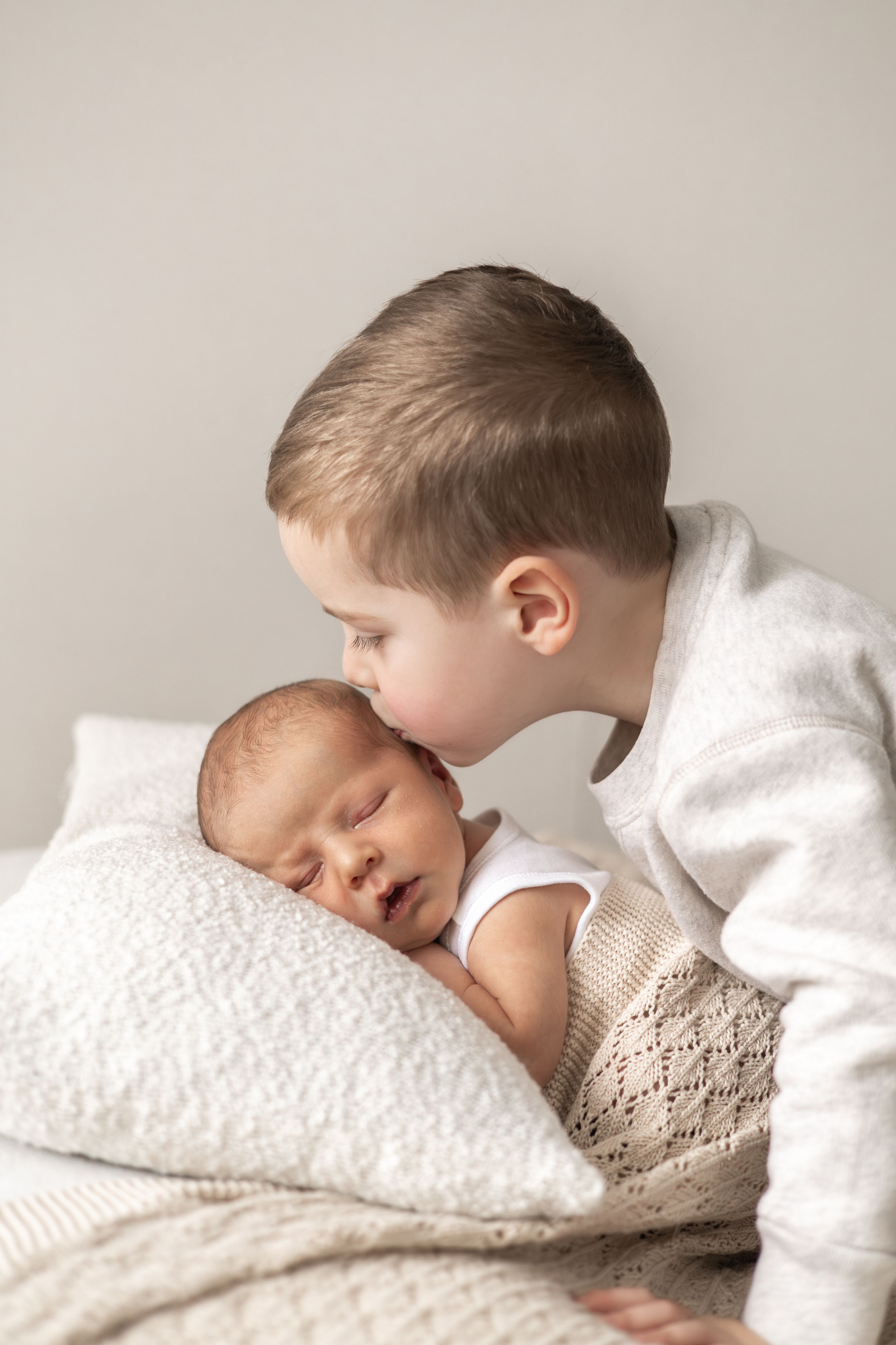 Young boy gently kissing sleeping newborn baby sibling newborn photography Nottingham simple timeless