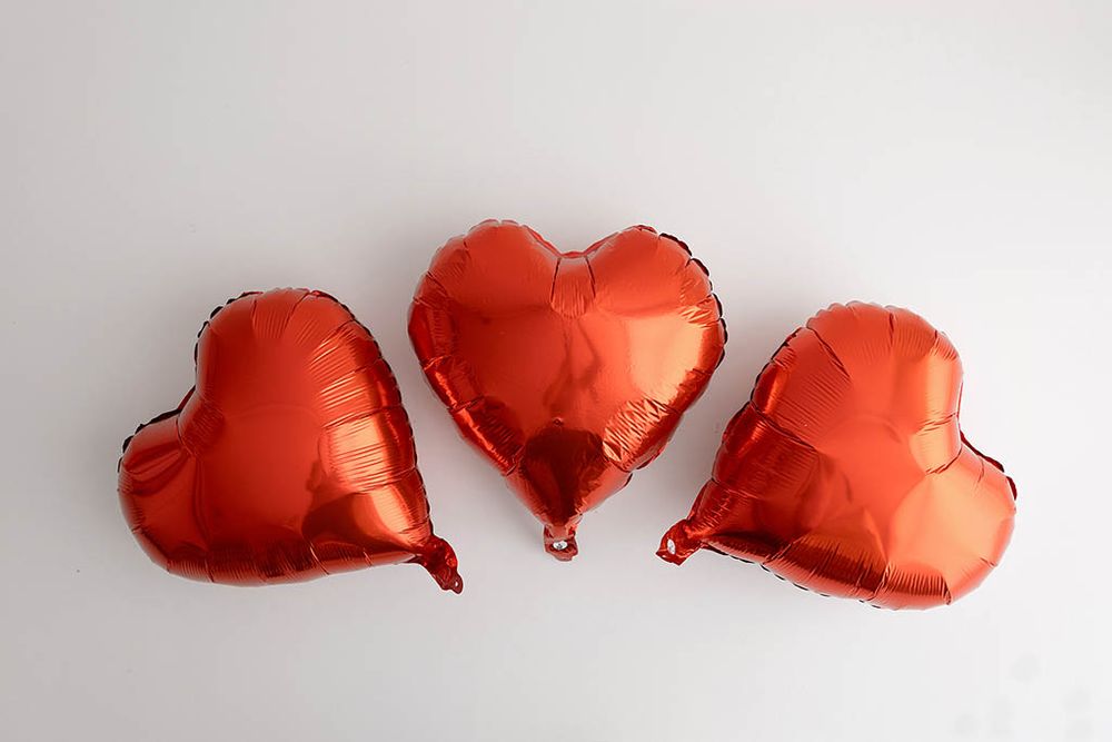 Three red heart-shaped foil balloons arranged on white background for Valentine's Day photoshoot in Temecula area.