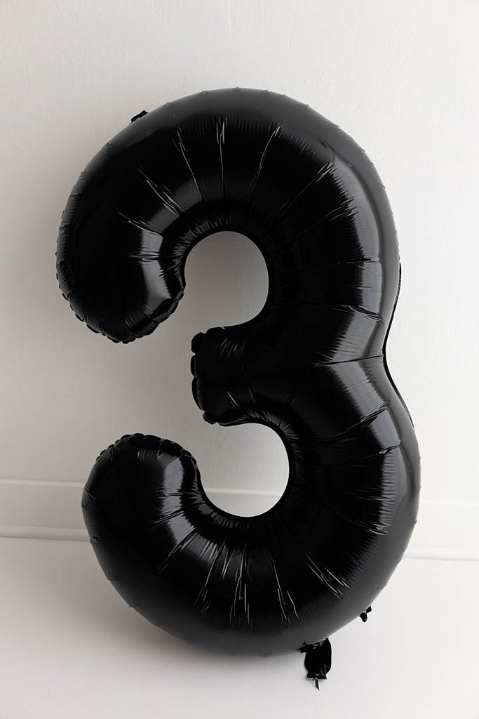 Black shiny number 3 foil balloon against a white background for 3rd birthday photoshoot in Murrieta CA.