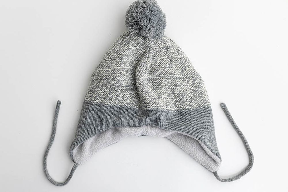 Gray marled knit baby hat with pom pom and ear flap ties.