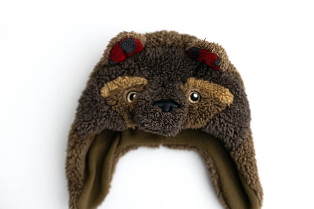Baby sized brown fuzzy bear trapper hat with red plaid ears for kids.