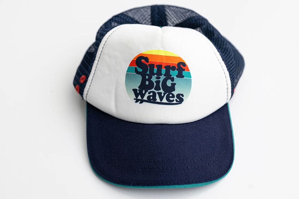 Baby boys navy blue trucker cap with colorful Surf Big Waves graphic patch on white background.