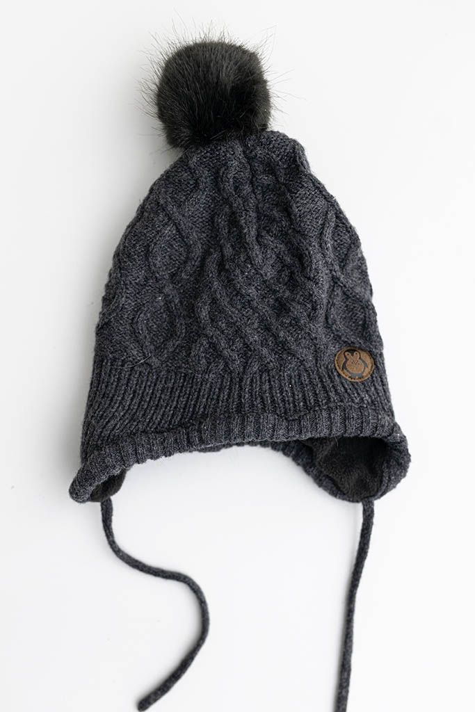 Dark gray cable knit baby hat with faux fur pompom and ear flap ties.