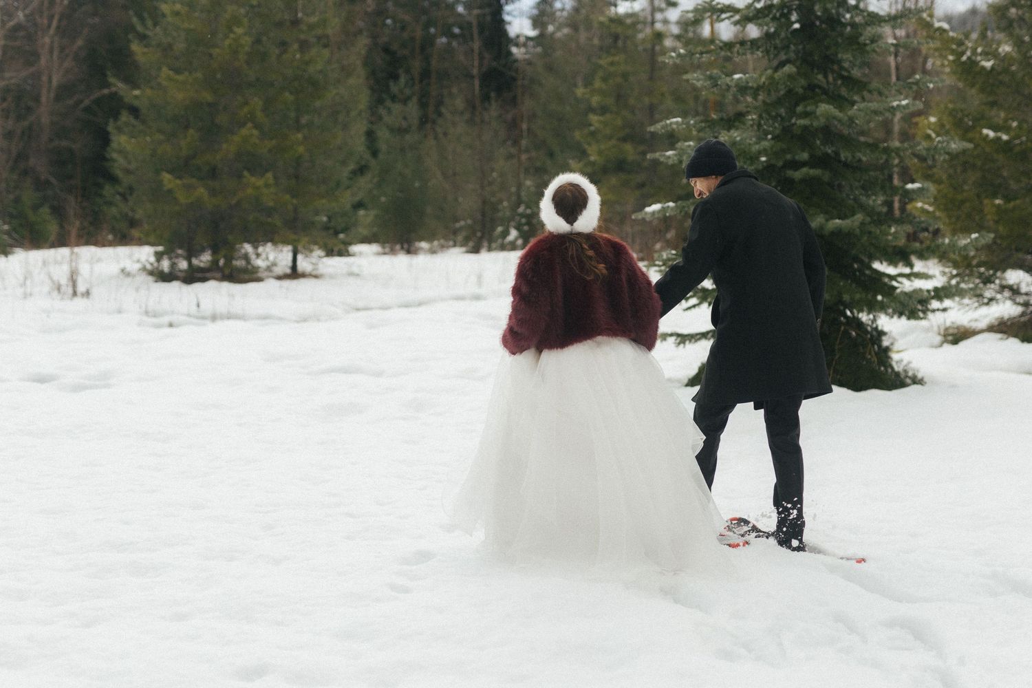 bride and groom snowshoe through a snowy forest in BC