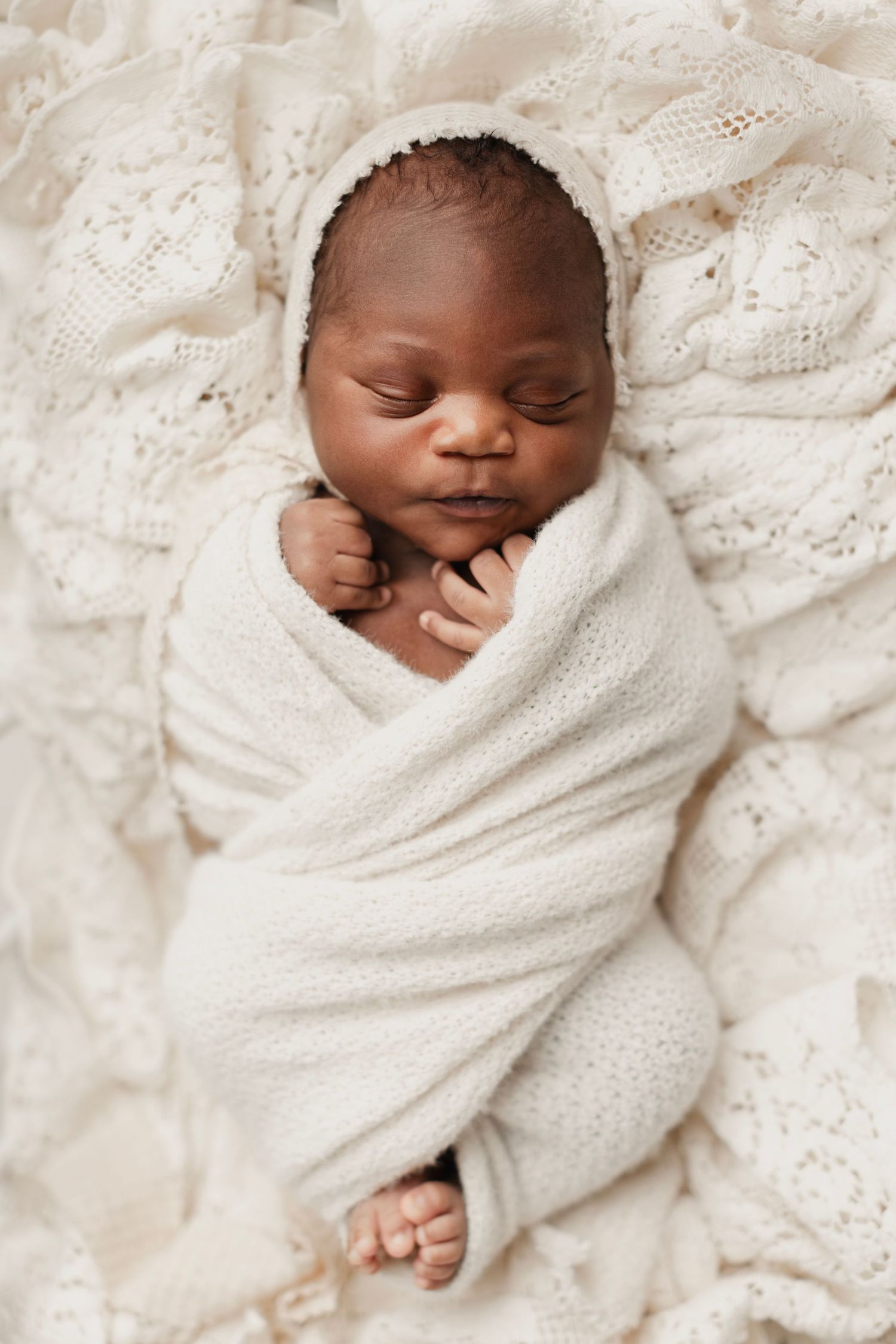 Peaceful newborn baby swaddled in cream white knit wrap sleeping on lace blanket. Elizabeth Lang Photography Surrey