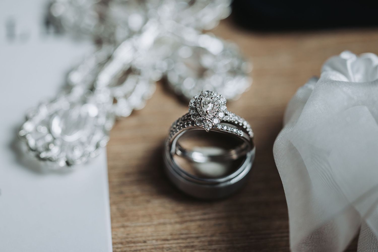 Close-up of bridal jewelry and wedding rings on a wooden surface, featuring a diamond halo engagement ring and men's wedding band.