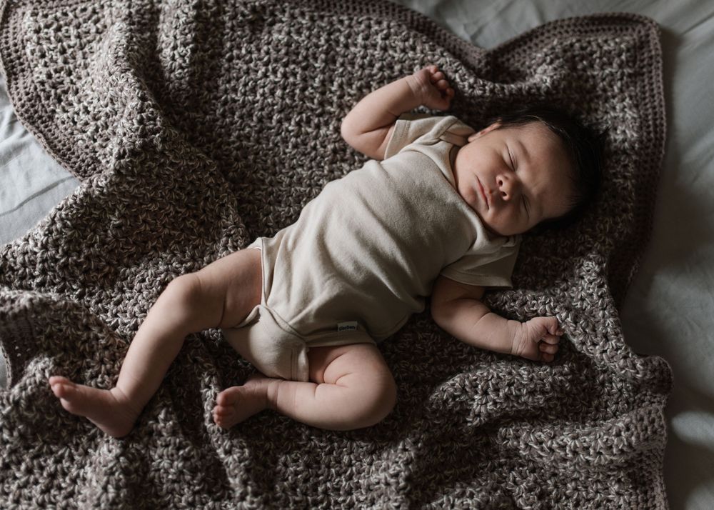 Peaceful newborn baby sleeping on a chunky knit brown blanket wearing a neutral linen onesie.