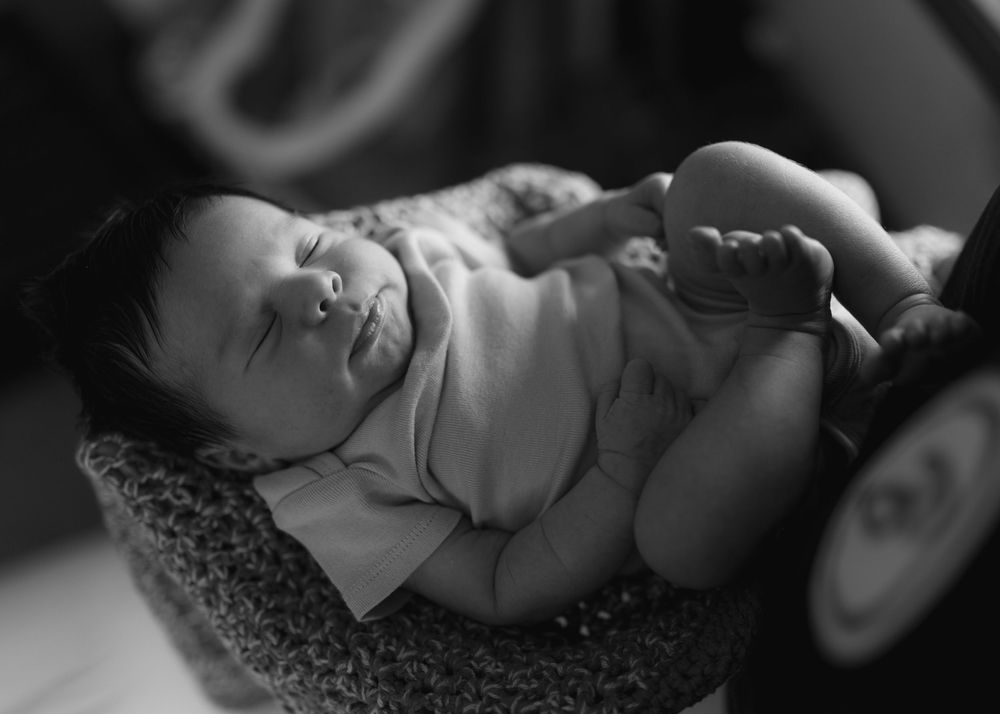 Black and white photo of a peaceful newborn baby sleeping curled up in a small basket.