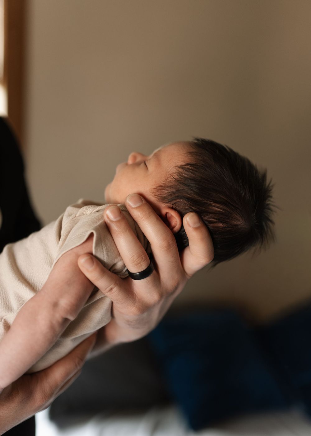 Adult hands gently cradling a sleeping newborn baby's head, wearing a black silicone ring.