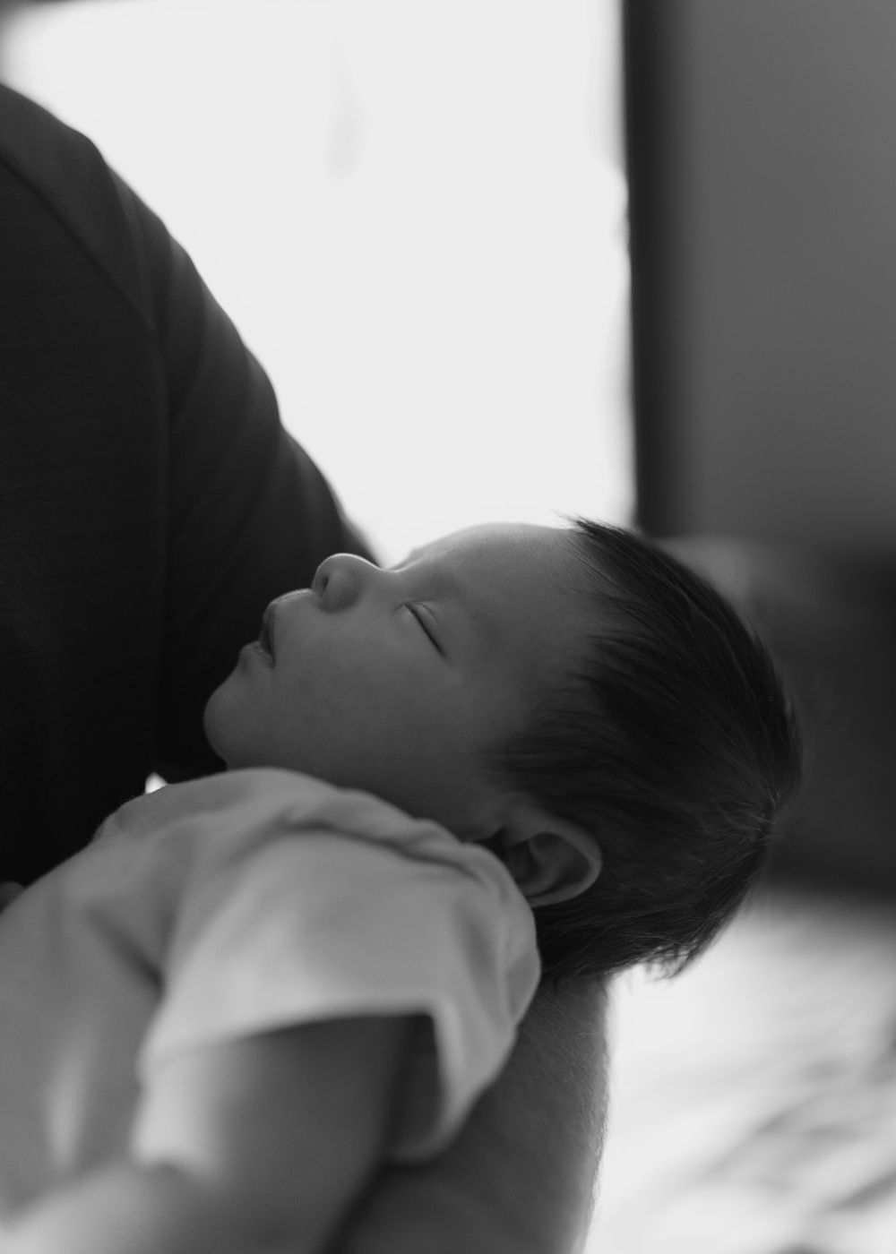 Black and white photo of a sleeping newborn baby cradled in an adult's arms, peaceful and serene.