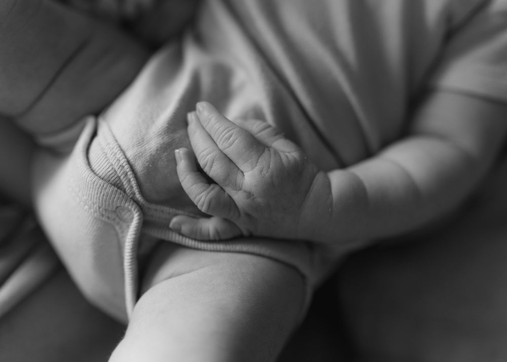 Black and white close-up of a newborn baby's tiny hand gently grasping an adult's finger.