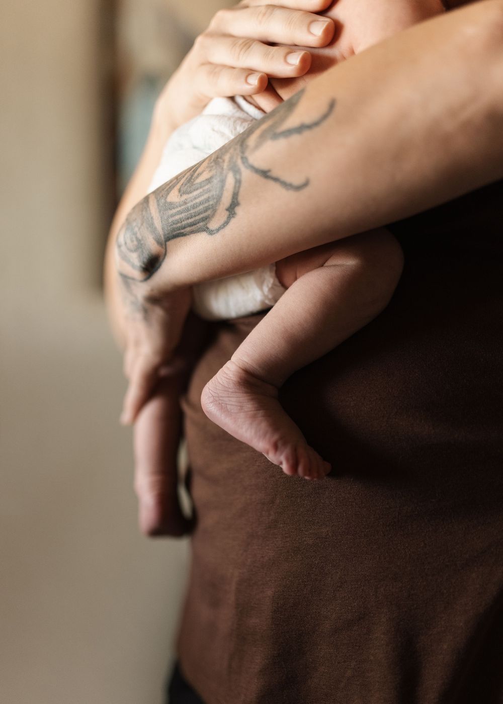 Tattooed parent holding a newborn baby against their chest in a tender embrace.