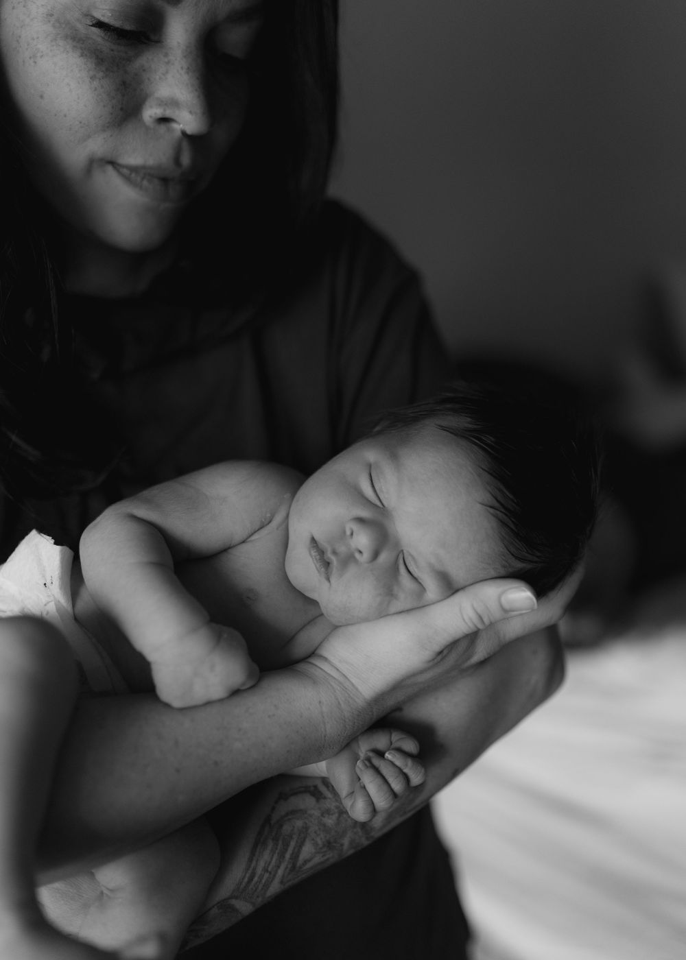 Black and white photo of a smiling mother tenderly cradling her sleeping newborn baby in her tattooed arms.