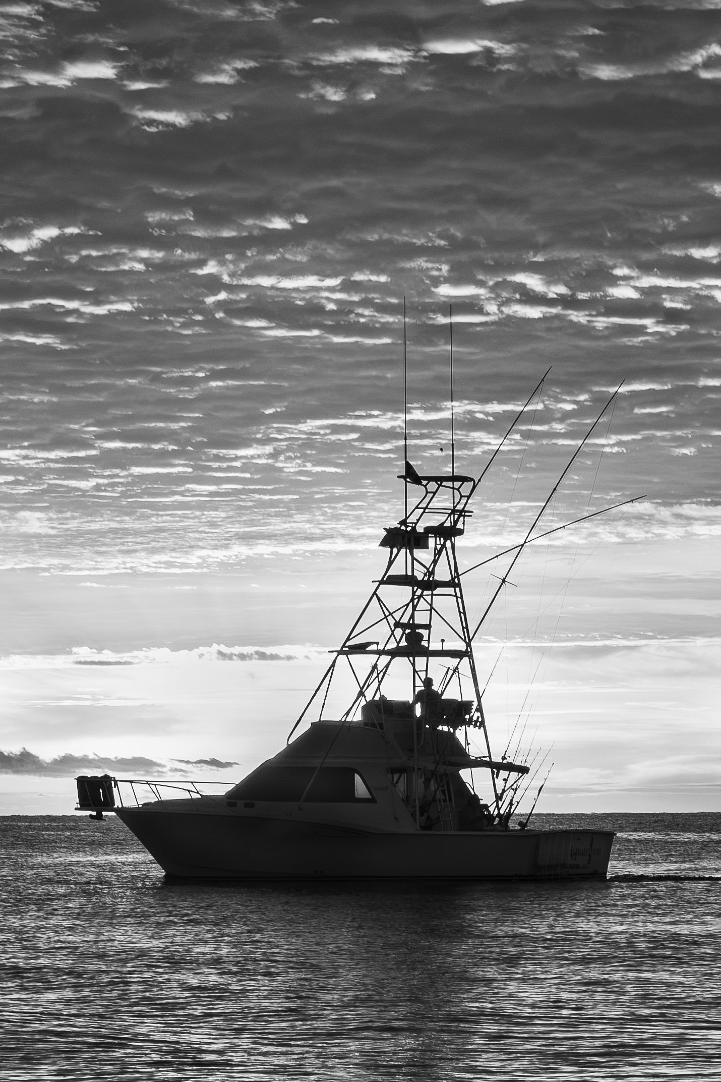 Black and white silhouette of a sport fishing boat anchored at sea under dramatic cloudy sky.