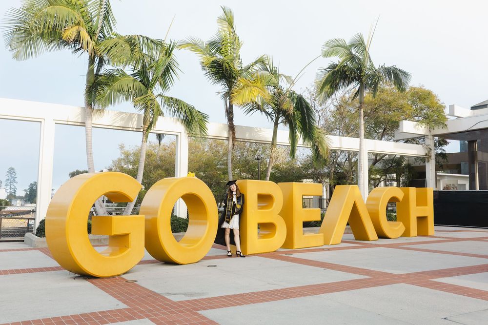 Student poses in front of large yellow GO BEACH sign with palm trees.