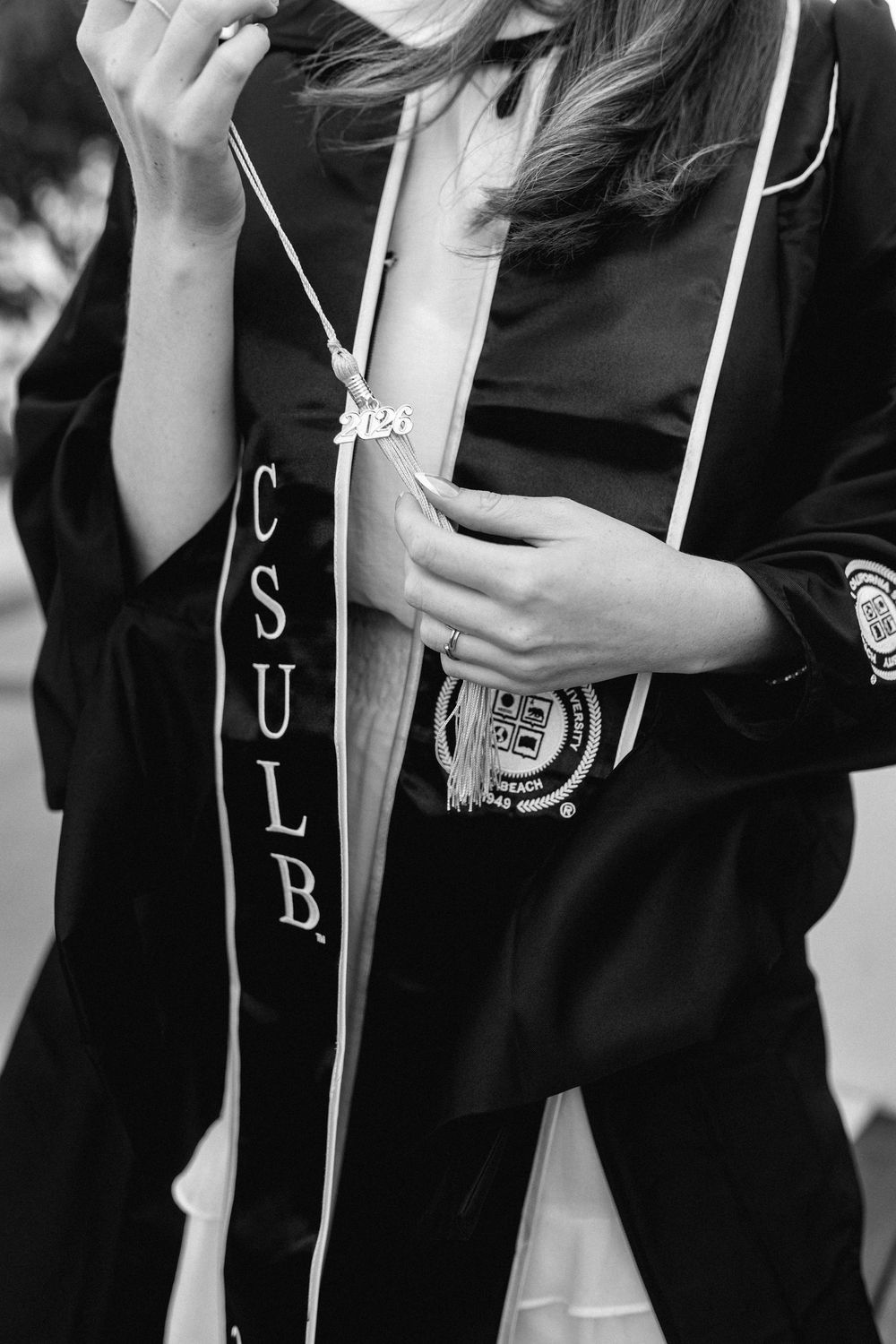 CSULB graduate in black cap and gown wearing graduation stole and tassel necklace, black and white photo.