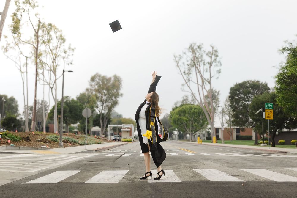 Graduate tosses cap in air while standing on crosswalk in cap and gown.