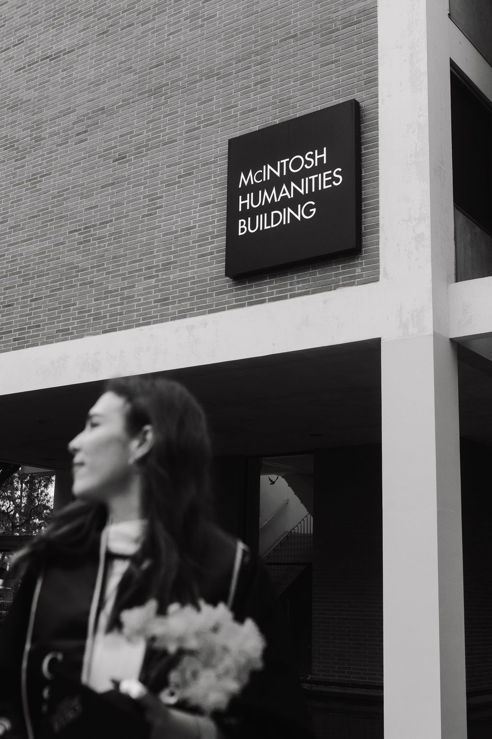 Black and white photo of woman holding flowers outside McIntosh Humanities Building.